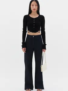Detail of a black ribbed knit cardigan with crossed waist ties and dark blue denim jeans
