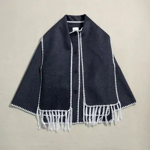 Detail of dark grey wool coat featuring white stitched edges and long fringe tassels