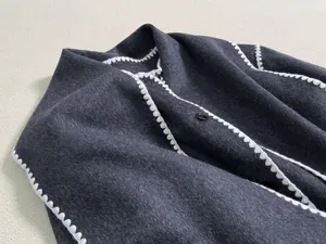 Detailed view of dark wool coat featuring distinctive white scalloped edge hand-stitching