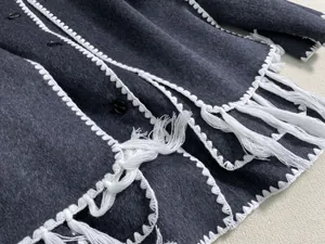 Detail of dark grey wool coat featuring white crochet edges and long fringe tassels