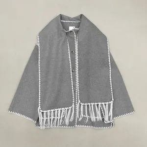 Detail of grey wool jacket featuring an integrated scarf with white zigzag embroidery and fringe