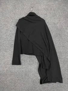 Detail of black asymmetrical knit top featuring long sleeves and a draped shawl detail