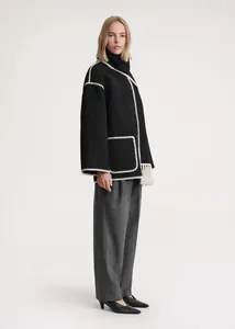 Detail view of black wool coat featuring white contrast stitching and woven fringe trim