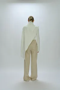 Rear view of cream long sleeve top with asymmetrical lace drape and wide leg trousers