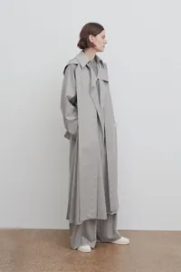 Détail d'un long trench-coat gris minimaliste avec une silhouette drapée de qualité