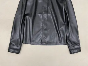 Detail of a black faux leather shirt sleeve with unique wavy stitching and round buttons