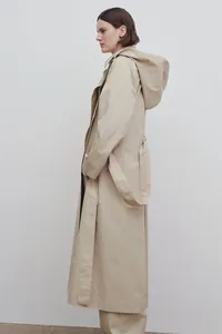 Side view of long khaki trench coat with detachable hood and waist belt detail
