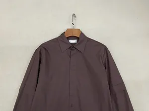 Dettaglio camicia in cotone marrone scuro con abbottonatura nascosta e maniche a strati