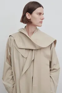 Detail of minimalist khaki trench coat with layered lapels and structured fabric texture