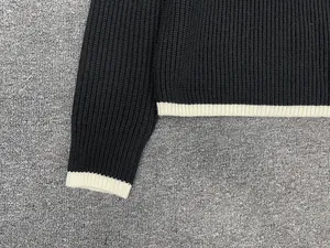 Detail of ribbed knit cuffs and hem with cream contrast edging on a black sweater