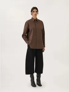 Dettaglio camicia in cotone marrone scuro a maniche lunghe e pantaloni neri a gamba larga