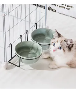 Close-up of dual hanging ceramic pet bowls in green with a black metal cage mount rack