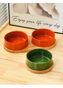 Close-up of ceramic pet bowls in vibrant orange and green with natural wooden tray stands