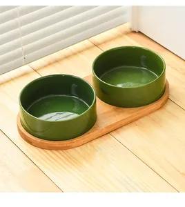 Close-up of dual dark green ceramic pet bowls on a natural bamboo elevated stand