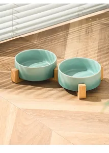 Dettaglio del supporto in legno rialzato con due ciotole in ceramica verde chiaro al sole