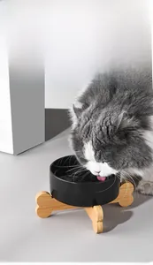 Matte black ceramic cat bowl on a bone-shaped wooden stand with a cat drinking water
