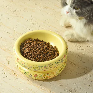 Gros plan d'un bol à chat en céramique jaune avec motifs graffiti et croquettes