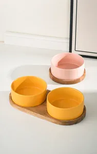 Detail of matte ceramic pet bowls in pink and yellow on acacia wood elevated trays