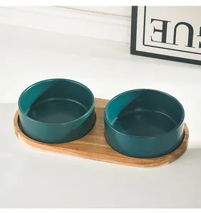 Close-up of dual dark green ceramic pet bowls with a natural acacia wood tray base