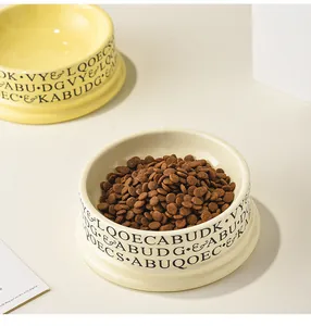 Detail of wide ceramic pet bowl with letter pattern and dry food for cats or dogs