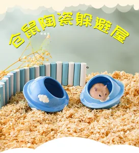 Blue ceramic UFO-shaped hamster hideout with white cloud patterns on soft wood bedding