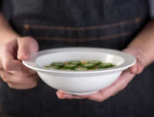 Primo piano di una ciotola per pasta in ceramica bianca tenuta con mani con zuppa