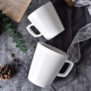 Top view of two white ceramic mugs with square handles on marble and linen background