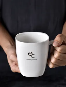 Nahaufnahme einer weißen Keramiktasse mit minimalistischem Logo, gehalten von zwei Händen