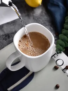 Action-Nahaufnahme beim Eingießen von Kaffee in einen quadratischen Keramikbecher