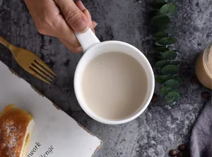 Close-up of a white ceramic coffee mug on a dark stone tabletop with a cozy breakfast scene