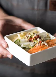 Close-up of a white square ceramic bowl with thick edges holding fresh vegetable side dishes