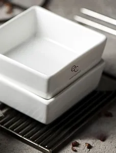 Macro detail of white square ceramic bowls showing premium glaze and branded logo design