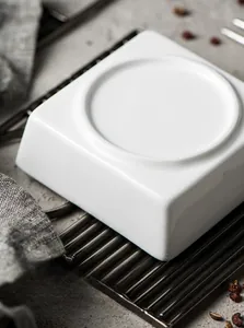 Detail of matte square ceramic bowl base with non-slip unglazed edge on dark rustic table