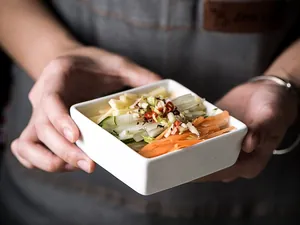 Macro shot of minimalist white square ceramic sauce dish held by hand in a kitchen setting