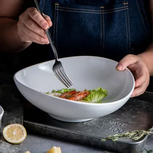 Close-up of hand holding a white irregular ceramic bowl with a rustic metal fork