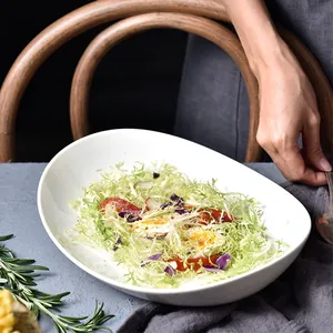 Minimalist white ceramic oval salad bowl with fresh vegetables on grey tablecloth