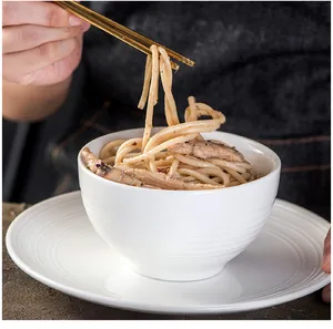 Detail of white ceramic dinnerware with horizontal ridges and golden chopsticks
