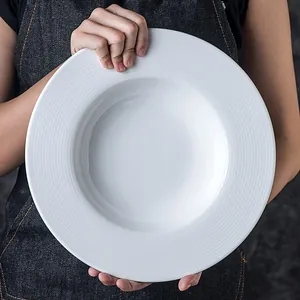 Minimalist white ceramic pasta plate with wide textured rim held by a person