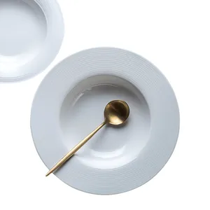 Minimalist white ceramic pasta plate with ripple pattern and matte gold spoon top view