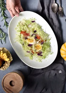 Detailansicht der hochwertigen weißen Keramikplatte mit frischem Salat und Kräutern