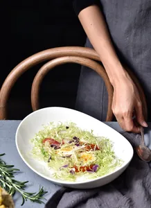 Tiefer ovaler Keramikteller mit verdicktem Rand für frischen Salat auf dem Esstisch