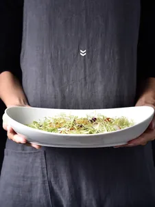 Detail einer weißen Keramikschale in Bootsform mit frischem Salat in den Händen
