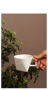 Detail of hand holding thick white ceramic coffee mug with geometric cone design