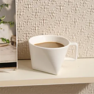 Minimalist white triangular ceramic coffee mug with square handle on a shelf