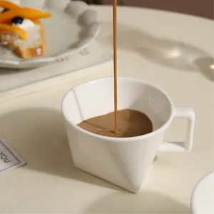 Unique triangular white ceramic coffee mug with geometric handle in minimalist setting