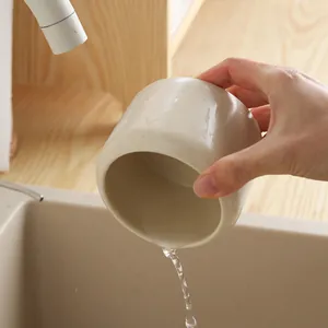 Minimalist ceramic cutlery holder in beige glaze being rinsed under a water faucet