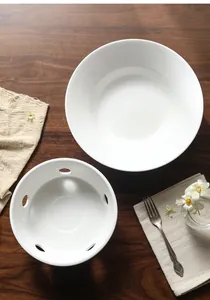 Top view of white ceramic soup bowl and warming stand on dark wood table with a linen cloth