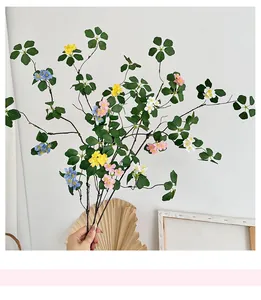 Detalle de hojas de loto zen artificiales y ramas con pequeñas flores multicolores
