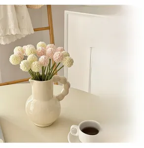 Artificial pink and cream pompom mums in a ceramic pitcher on a minimalist table