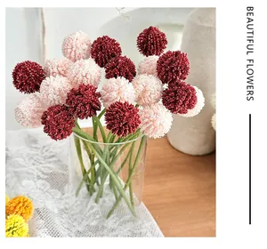 Detail of burgundy and pink spherical faux flowers in a clear glass vase on a wooden table